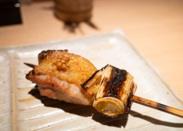 Yakitori at Yakitori Omino, with a grilled piece of chicken and leek on a skewer. They look slightly charred..